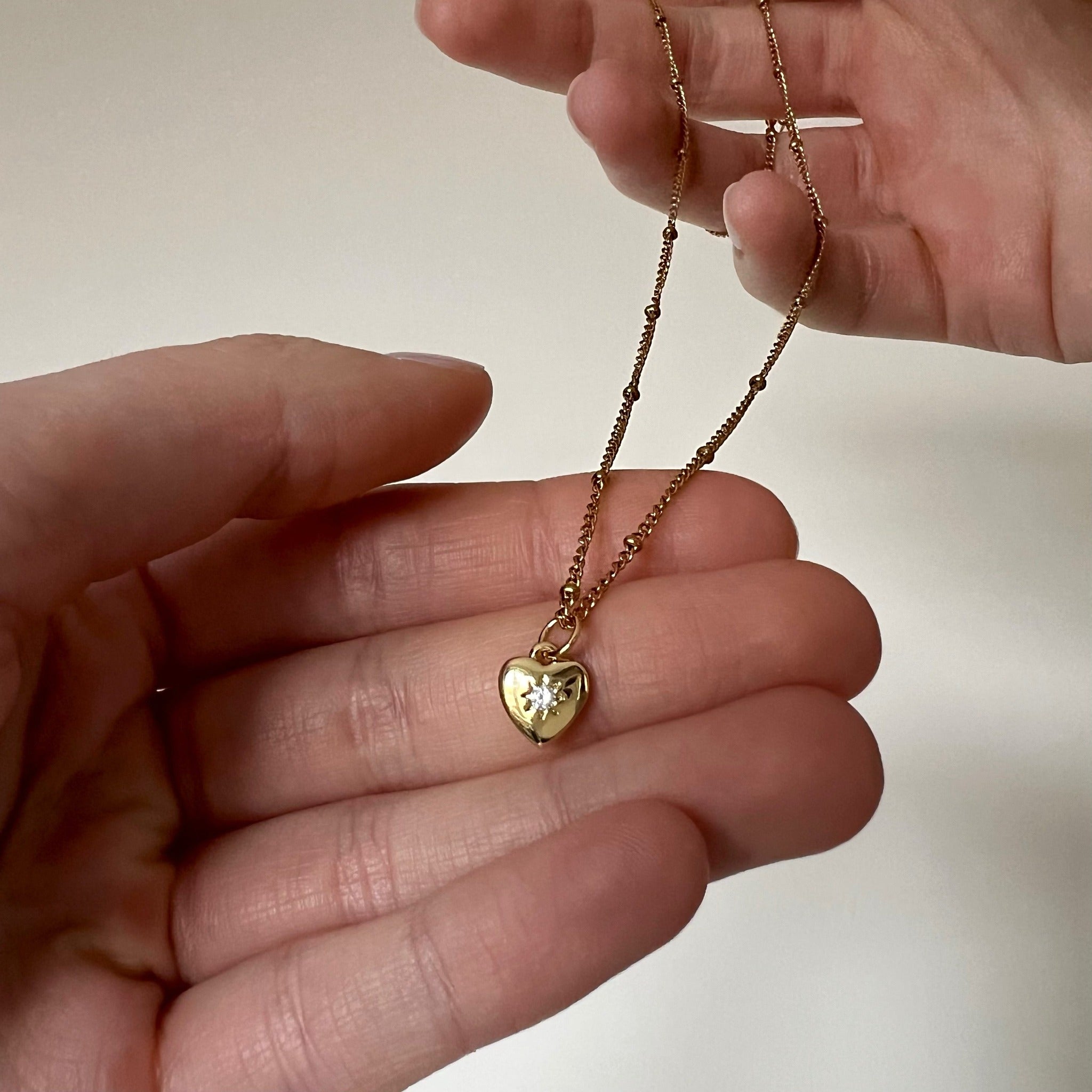 Minimalistyczny złoty naszyjnik z zawieszką w kształcie serca, w której znajduje się cyrkonia w kształcie gwiazdki.